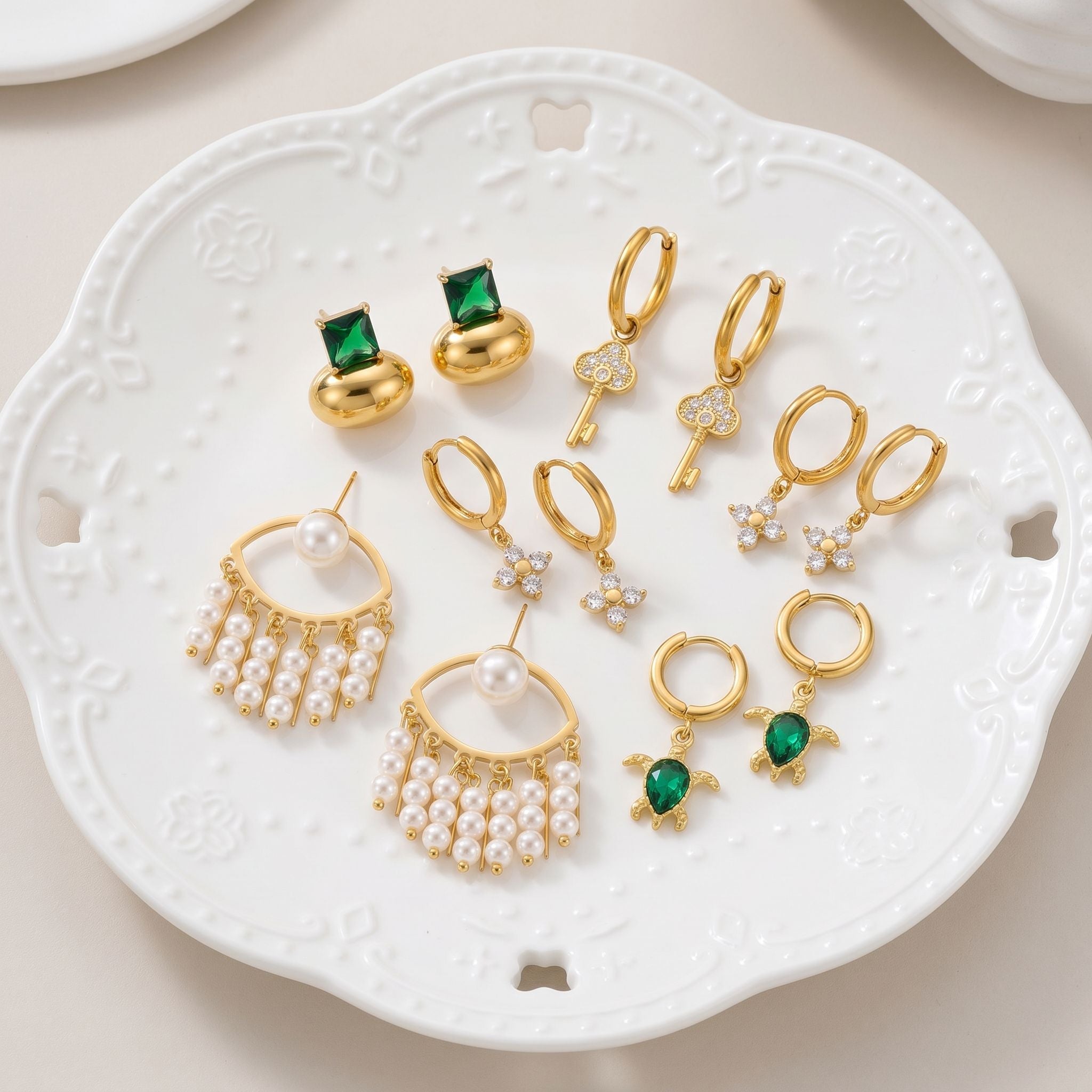 Pair of shiny gold geometric hoop earrings on textured fabric with green jewelry box