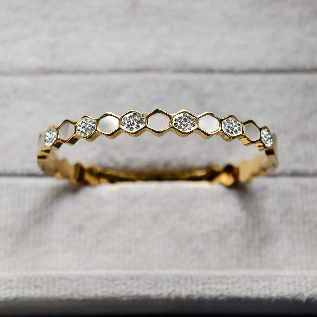 Close-up of gold honeycomb bracelet with embedded crystals on gray fabric background