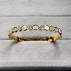 Close-up of gold honeycomb bracelet with embedded crystals on gray fabric background