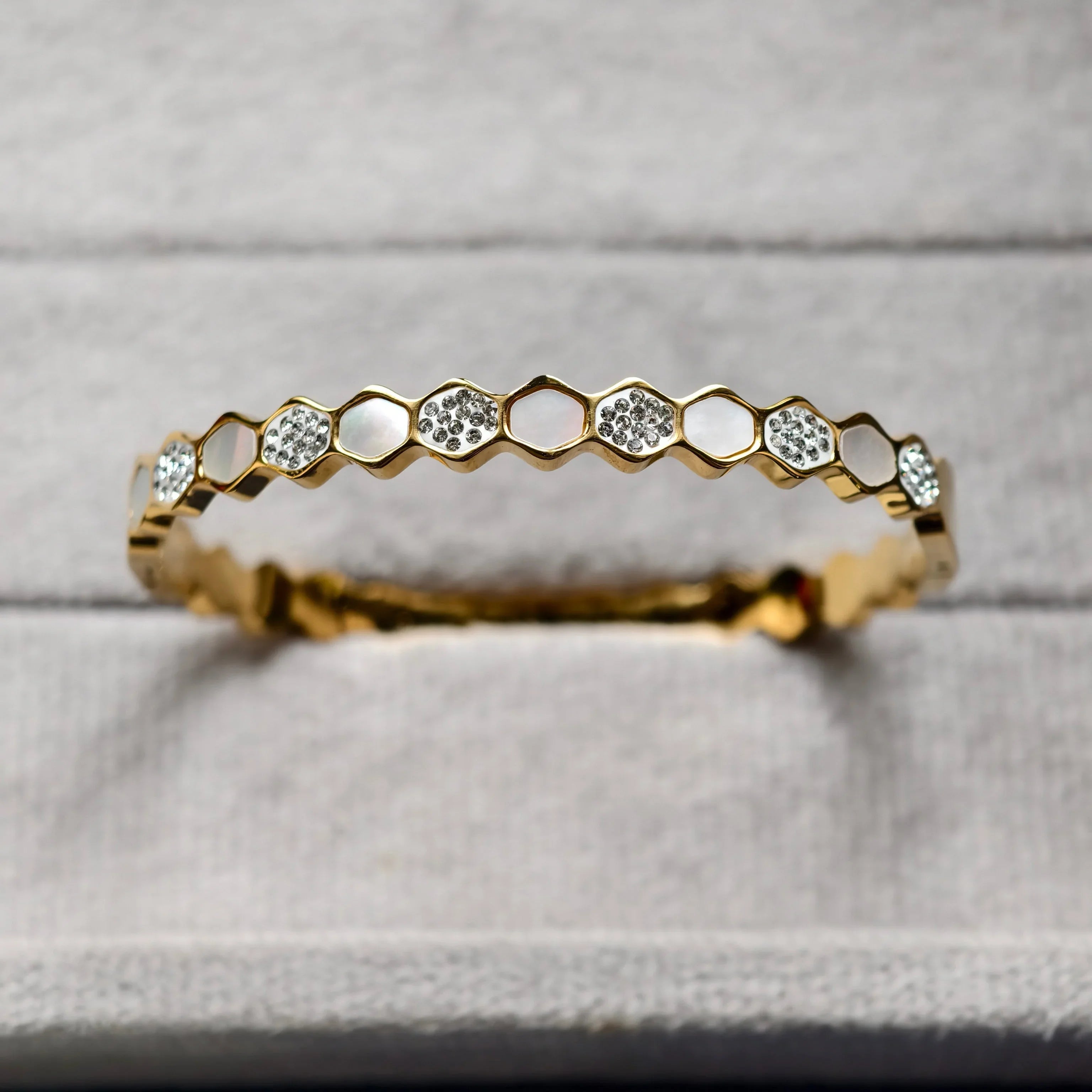 Close-up of gold honeycomb bracelet with embedded crystals on gray fabric background