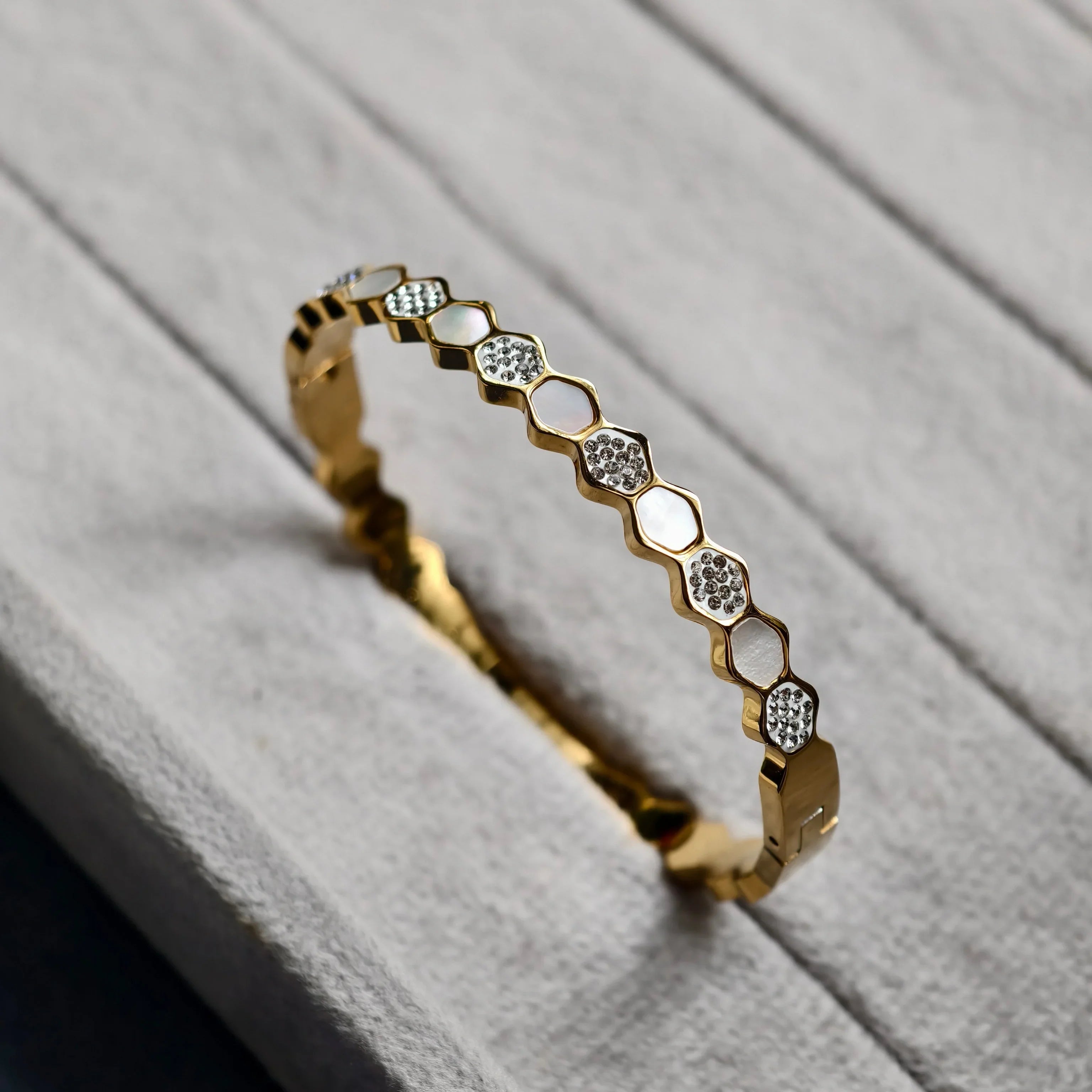 Gold bracelet with hexagonal links featuring mother-of-pearl and crystal accents on textured surface