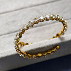Gold tennis bracelet with round clear gemstones on a textured light surface
