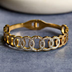 Gold bracelet with interlocking circular links embellished with clear rhinestones on gray surface