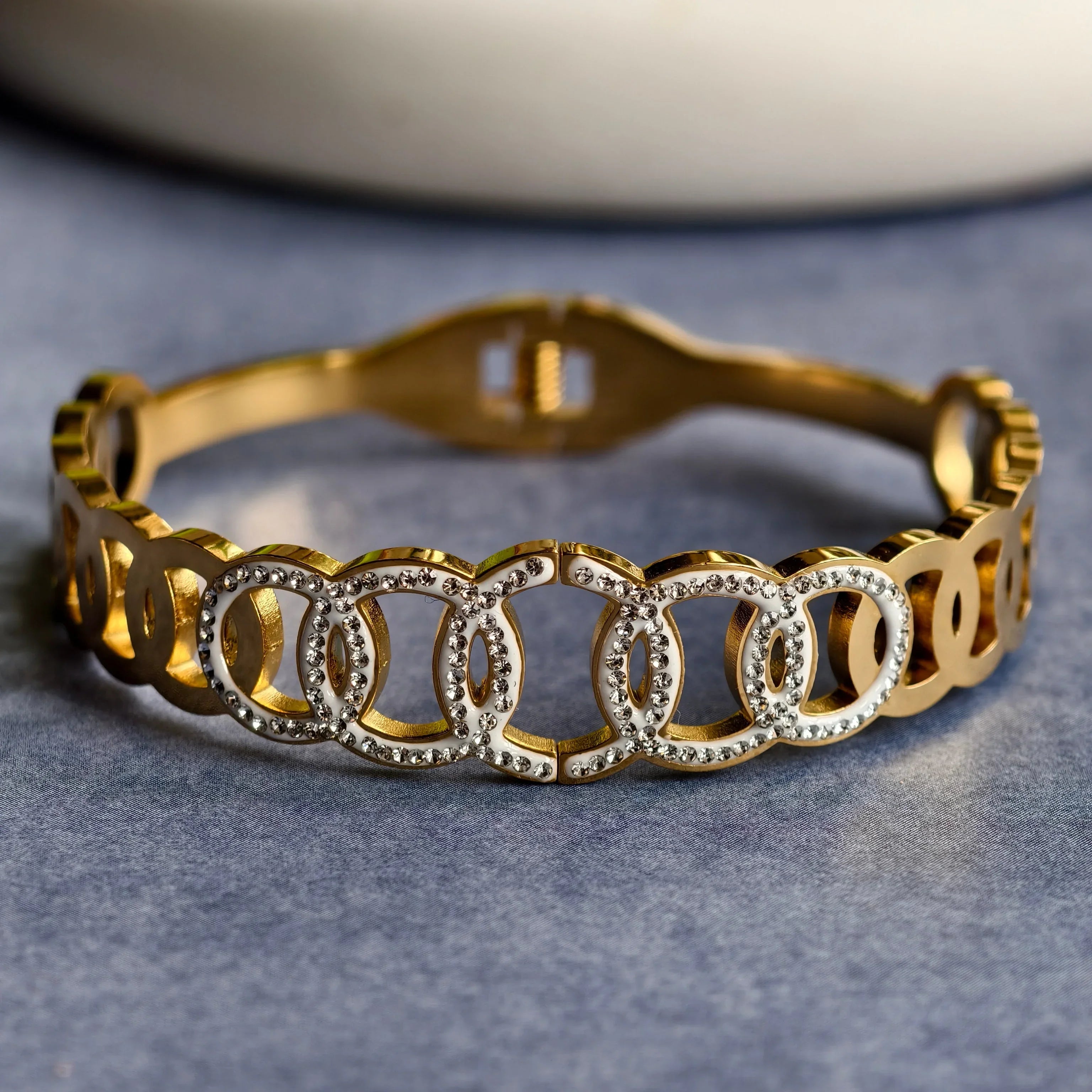 Gold bracelet with interlocking circular links embellished with clear rhinestones on gray surface