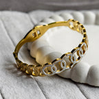 Gold bracelet with interlocking circle design accented with small clear crystals on a soft textured surface