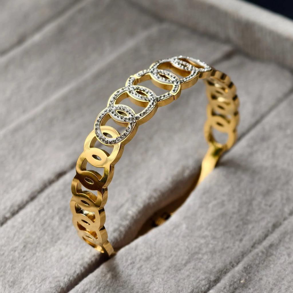 Gold bracelet with linked oval shapes, some decorated with small white stones, on gray cushion