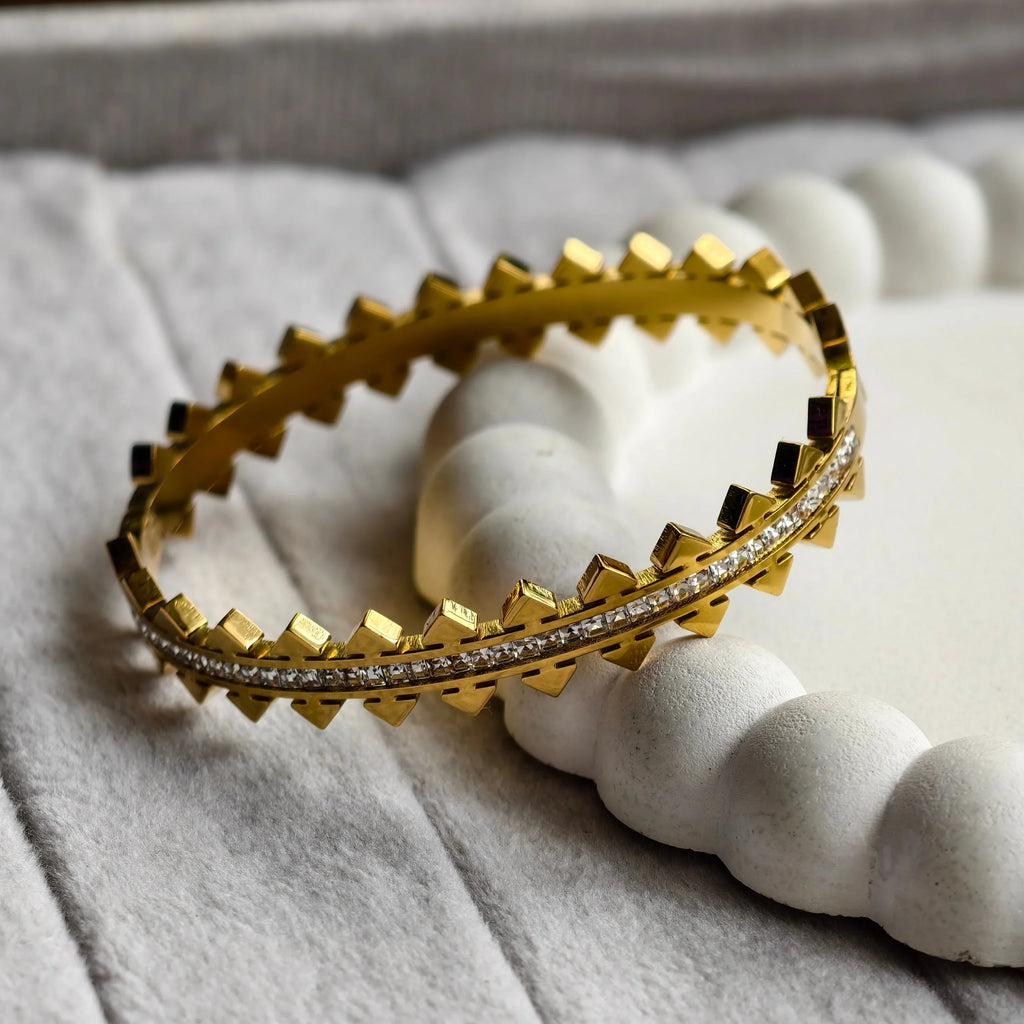 Gold bracelet with pyramid studs and embedded clear stones on textured white surface