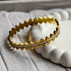 Gold bracelet with pyramid studs and embedded clear stones on textured white surface