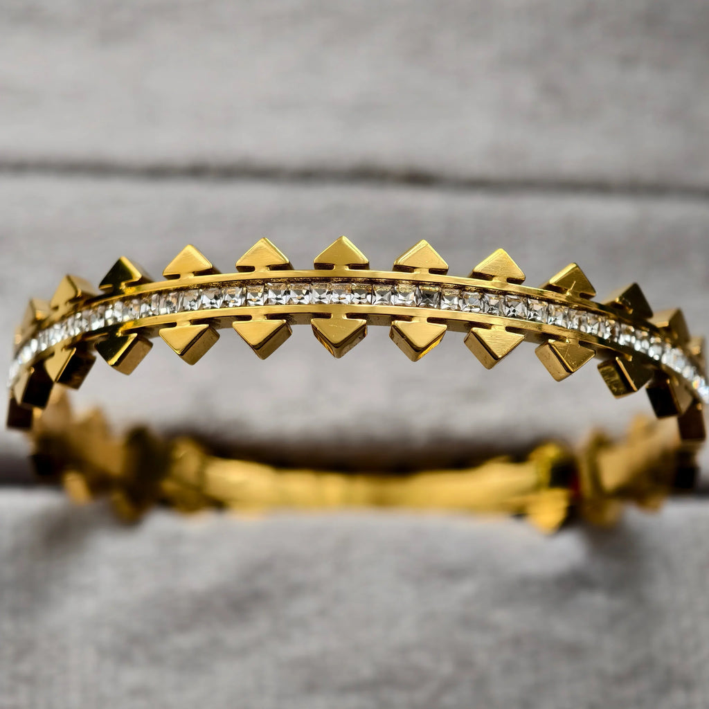 Gold bracelet with pyramid studs and row of clear square gemstones on gray background