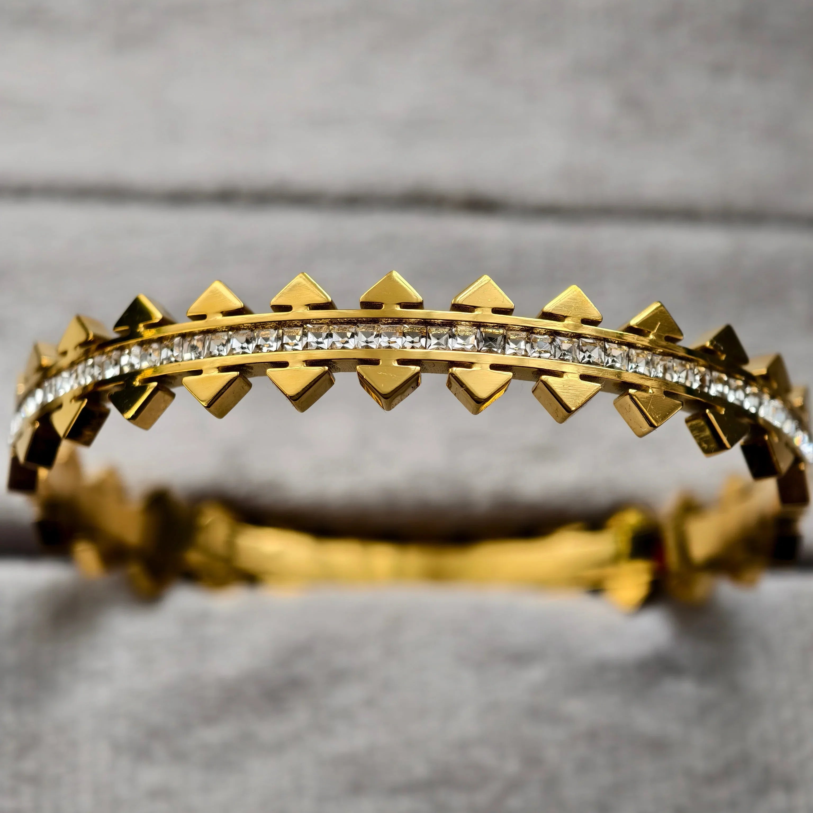 Gold bracelet with pyramid studs and row of clear square gemstones on gray background