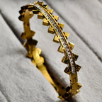 Gold bracelet with pyramid studs and a row of clear crystals on a grey fabric background