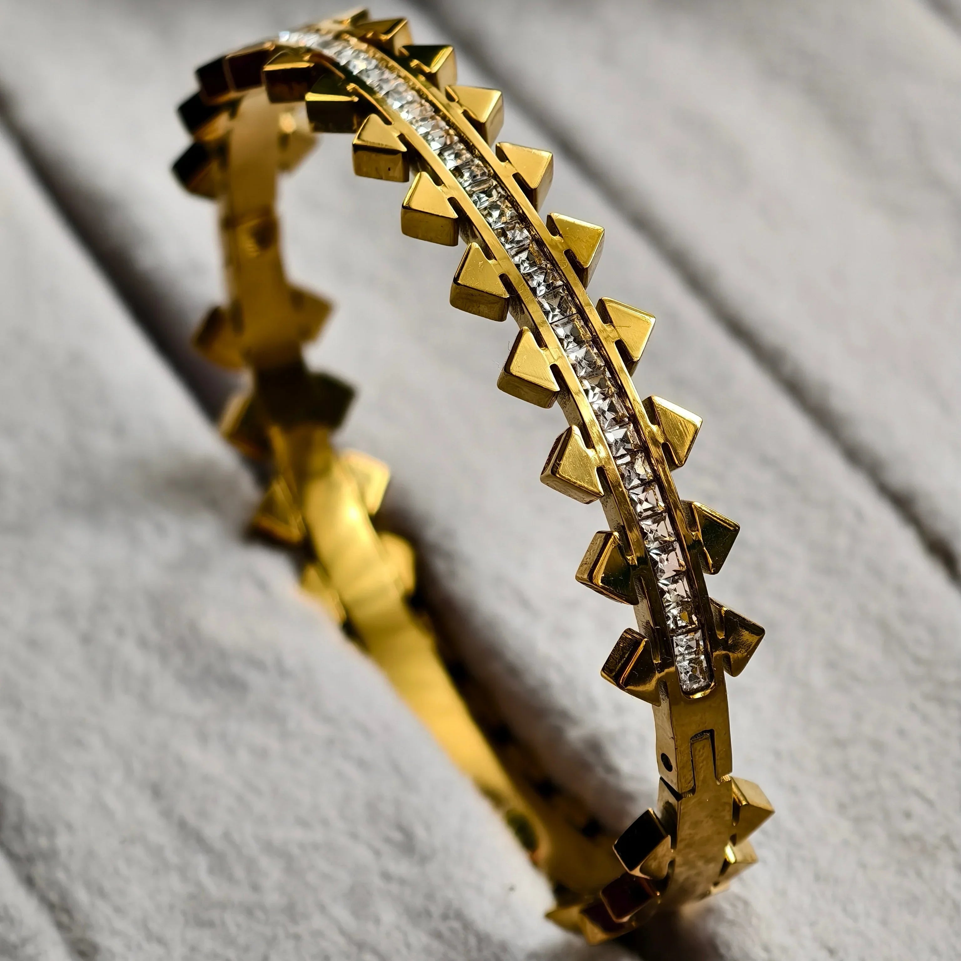 Gold bracelet with pyramid studs and a row of clear crystals on a grey fabric background