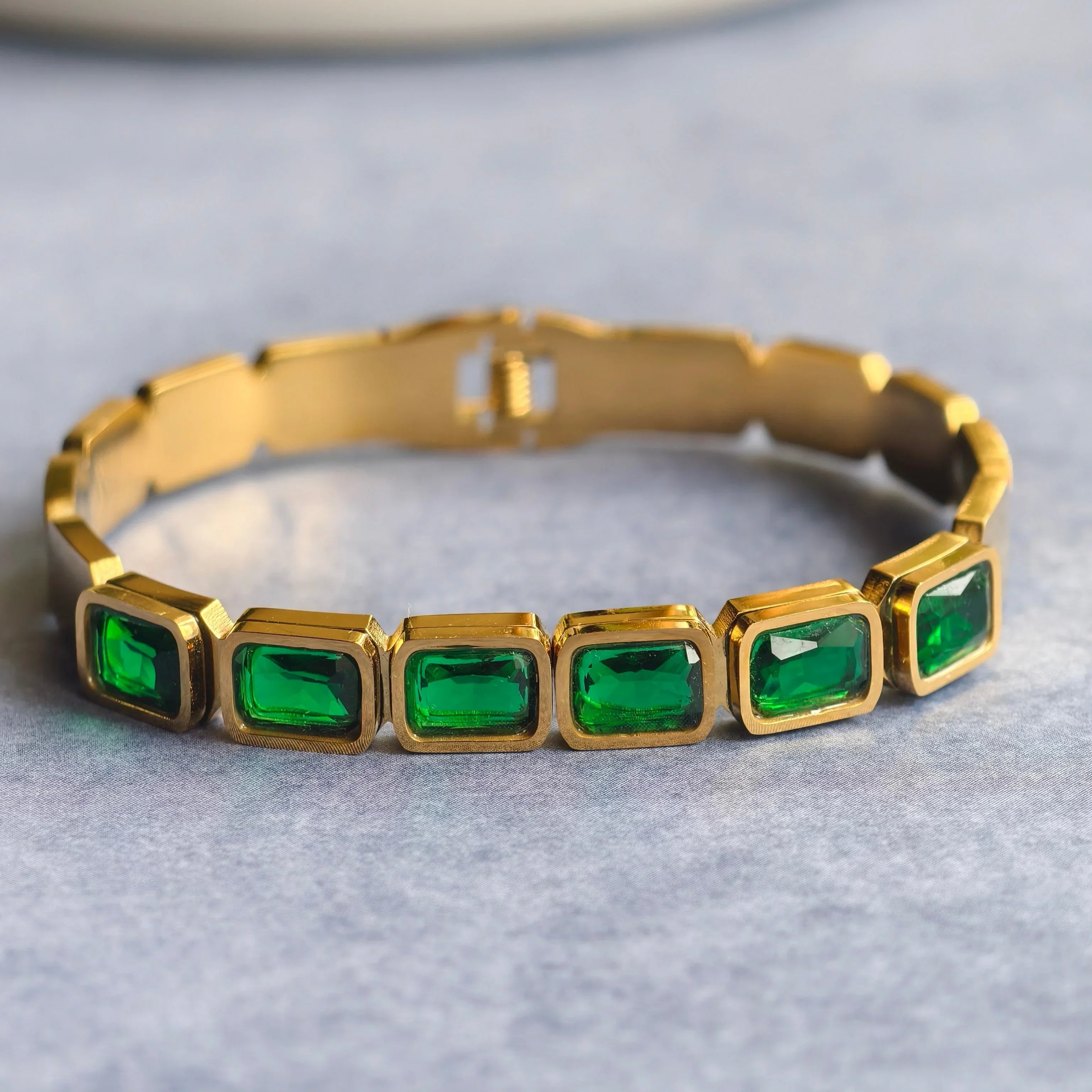 Gold bracelet with rectangular green gemstones on gray surface