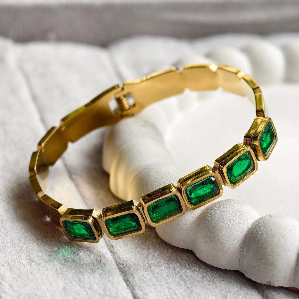 Gold bracelet with six rectangular green gemstones on white textured surface