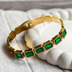 Gold bracelet with six rectangular green gemstones on white textured surface