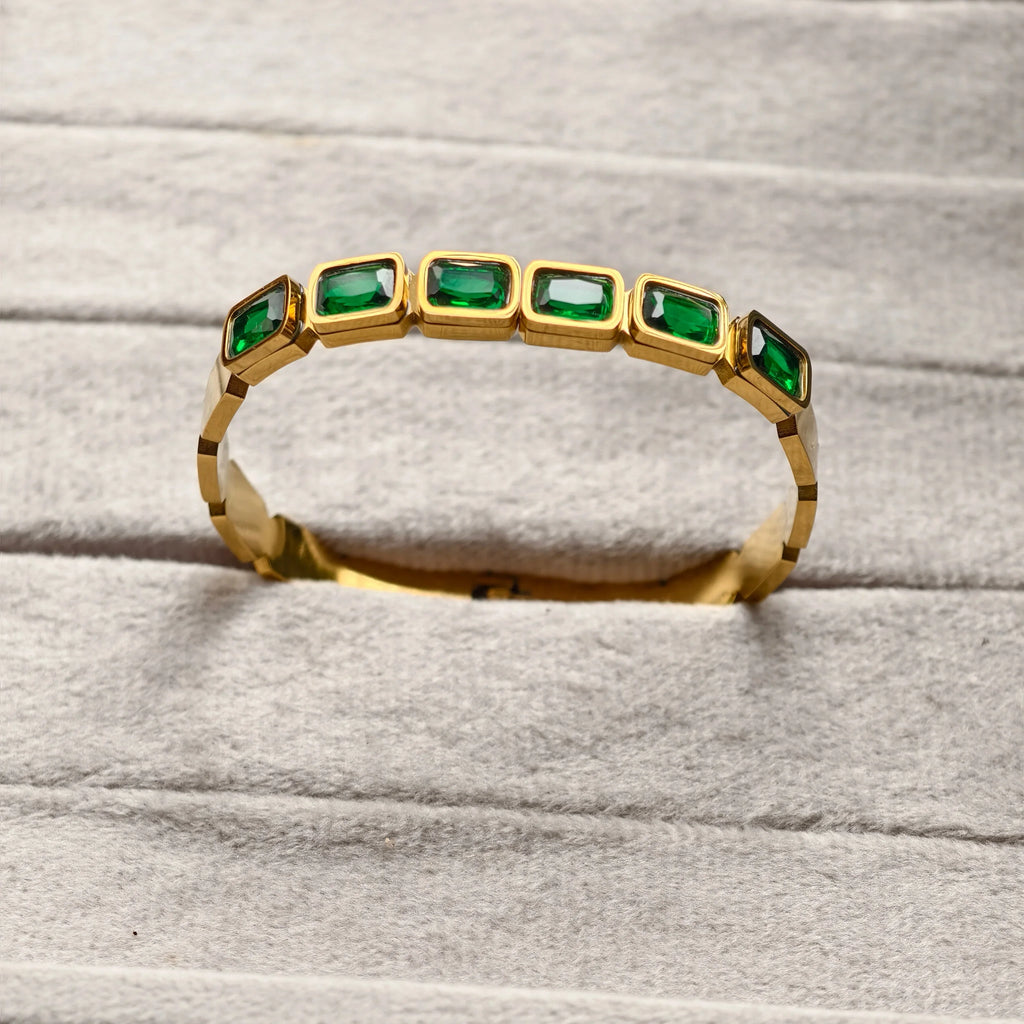 Gold bracelet with rectangular green gemstones on soft gray fabric background