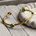 Gold bangle bracelet with green and clear oval gemstones on soft textured surface