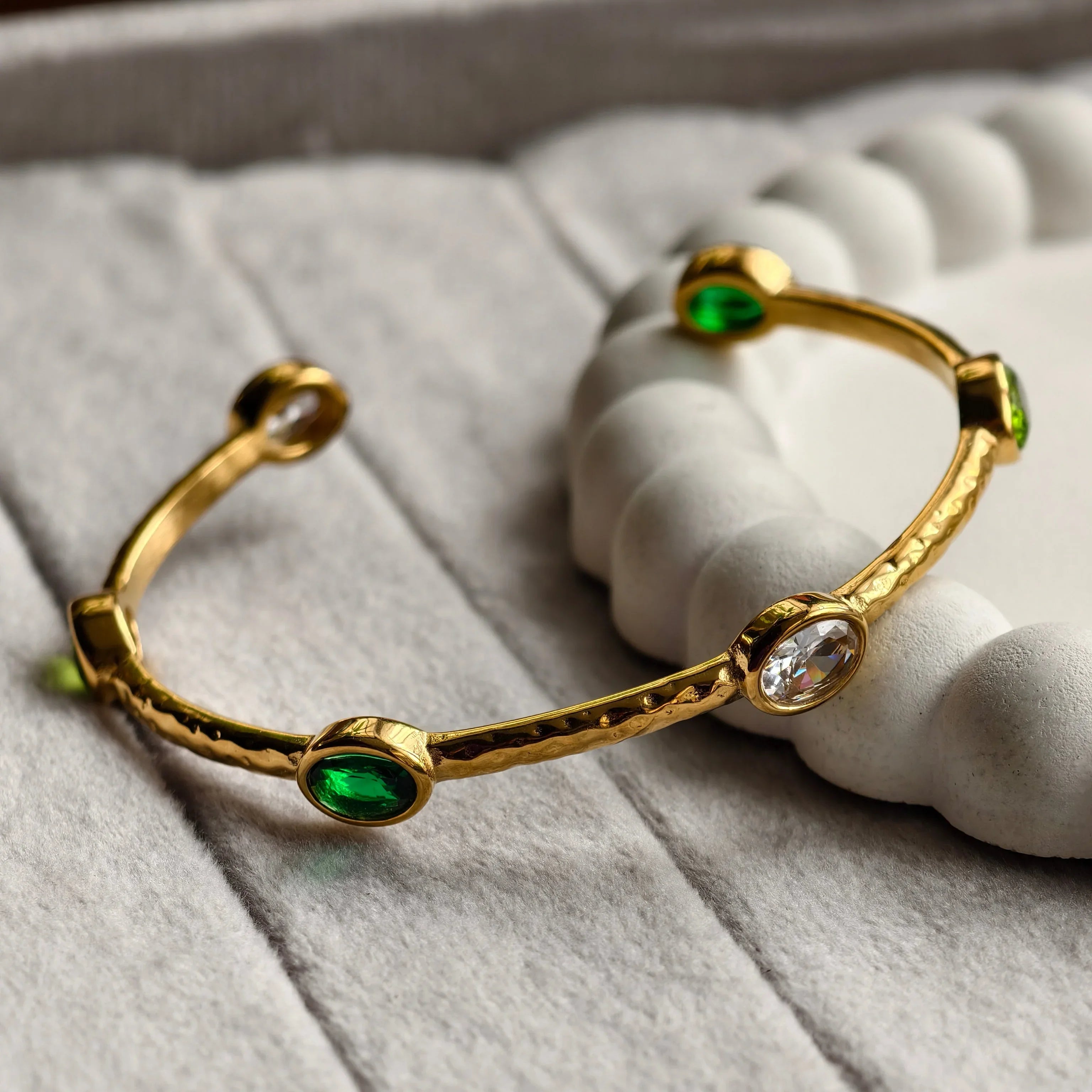 Gold bangle bracelet with green and clear oval gemstones on soft textured surface