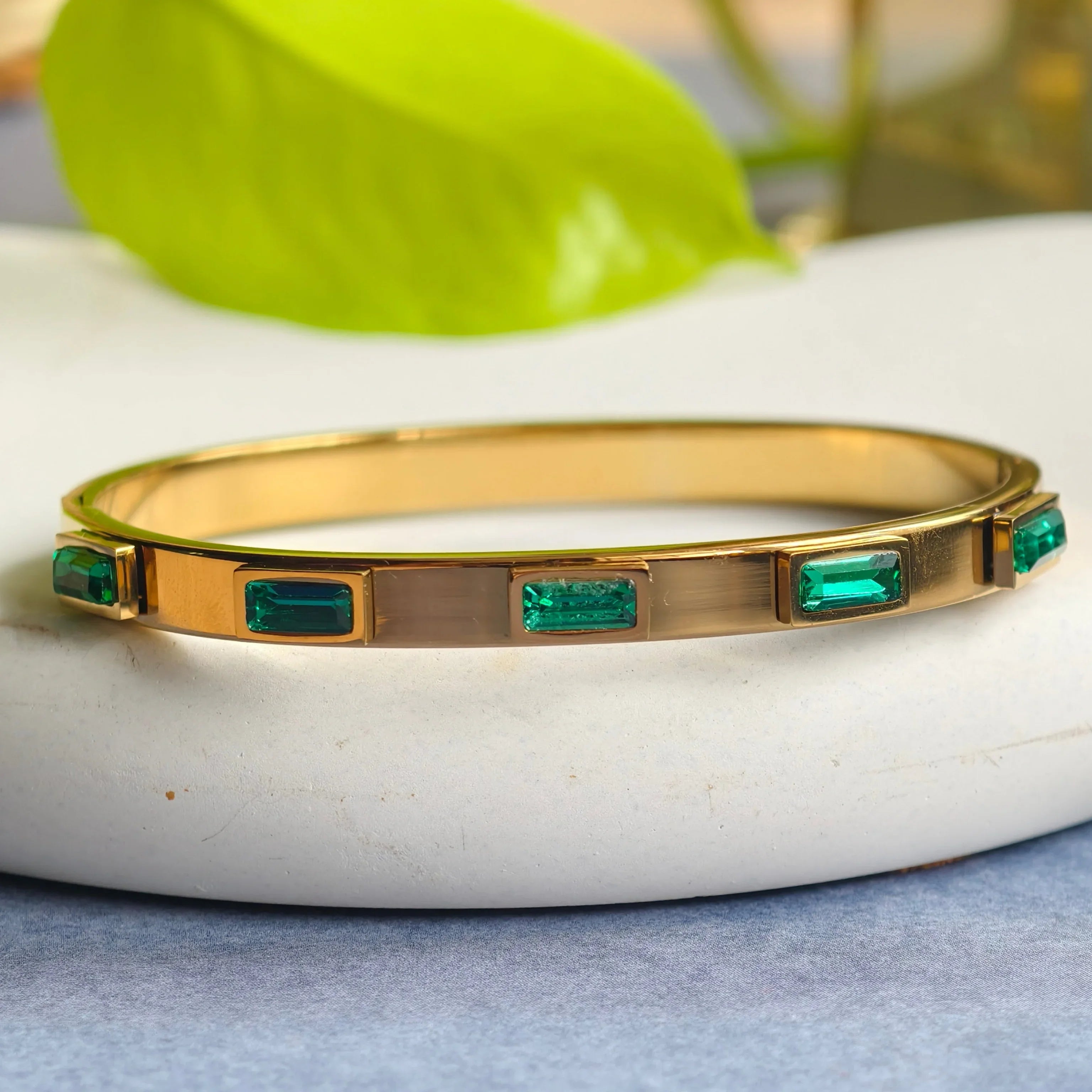 Gold bangle bracelet with rectangular emerald green gemstones on white surface
