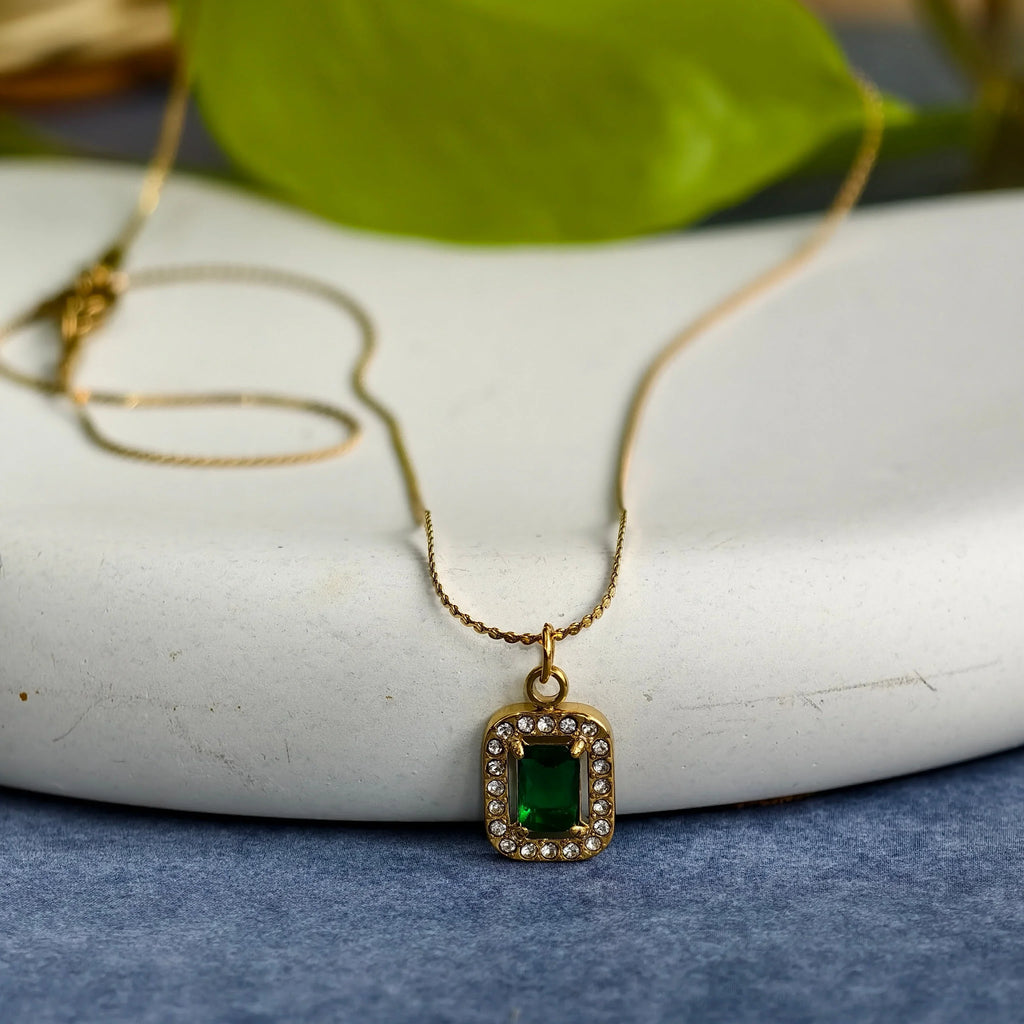 Gold pendant necklace with rectangular green gemstone surrounded by small clear crystals