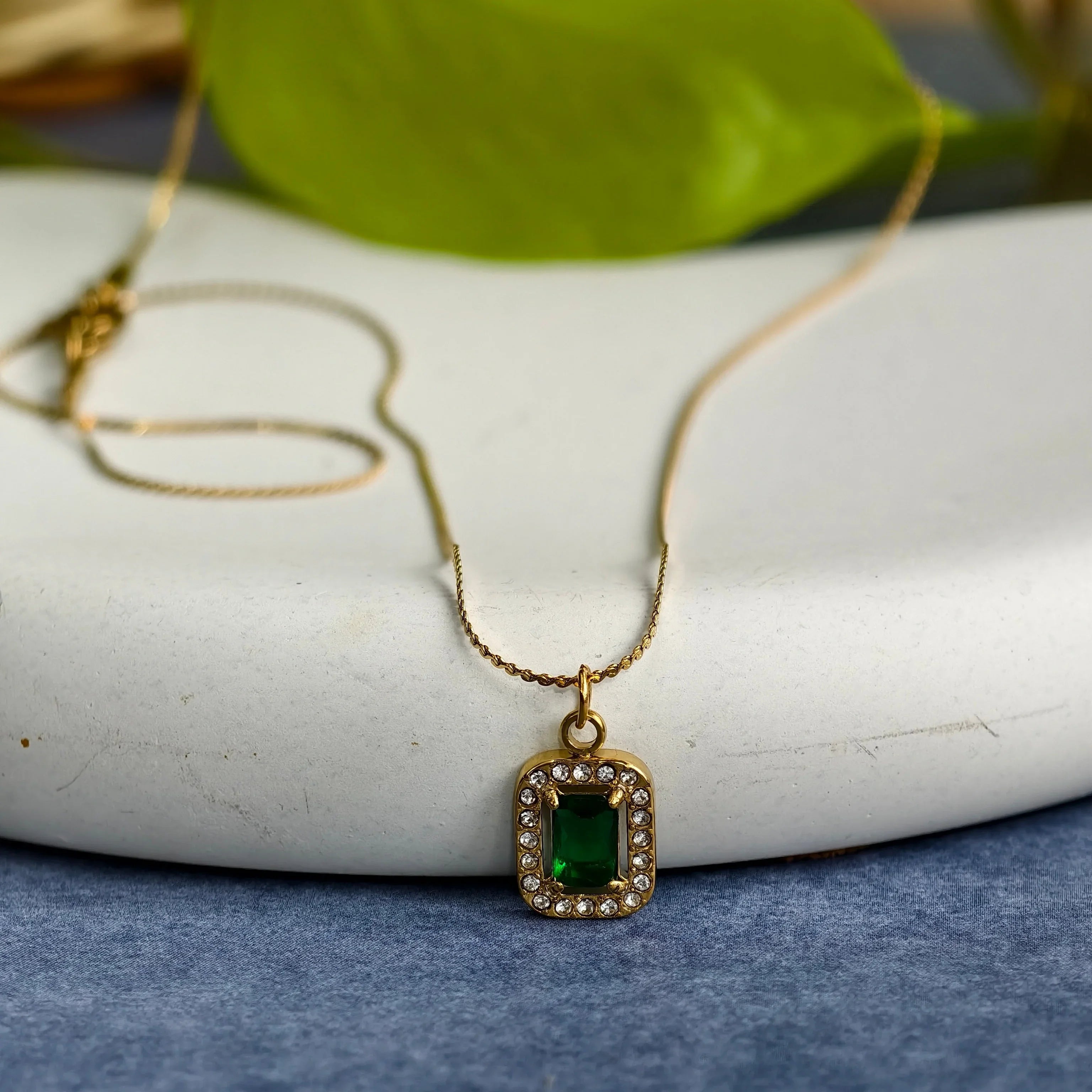 Gold pendant necklace with rectangular green gemstone surrounded by small clear crystals