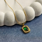 Gold necklace with emerald center stone surrounded by clear crystals on blue surface