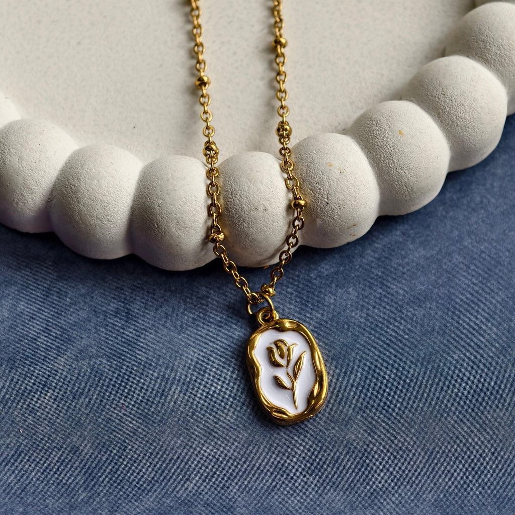 Gold chain necklace with a white and gold flower pendant resting on a textured white decorative plate and blue fabric background