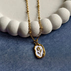 Gold chain necklace with a white and gold flower pendant resting on a textured white decorative plate and blue fabric background