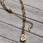 Gold chain necklace with white enamel pendant featuring a floral design on soft gray fabric