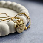 Gold locket pendant with crescent moon and star crystals on a chain, placed on white textured tray