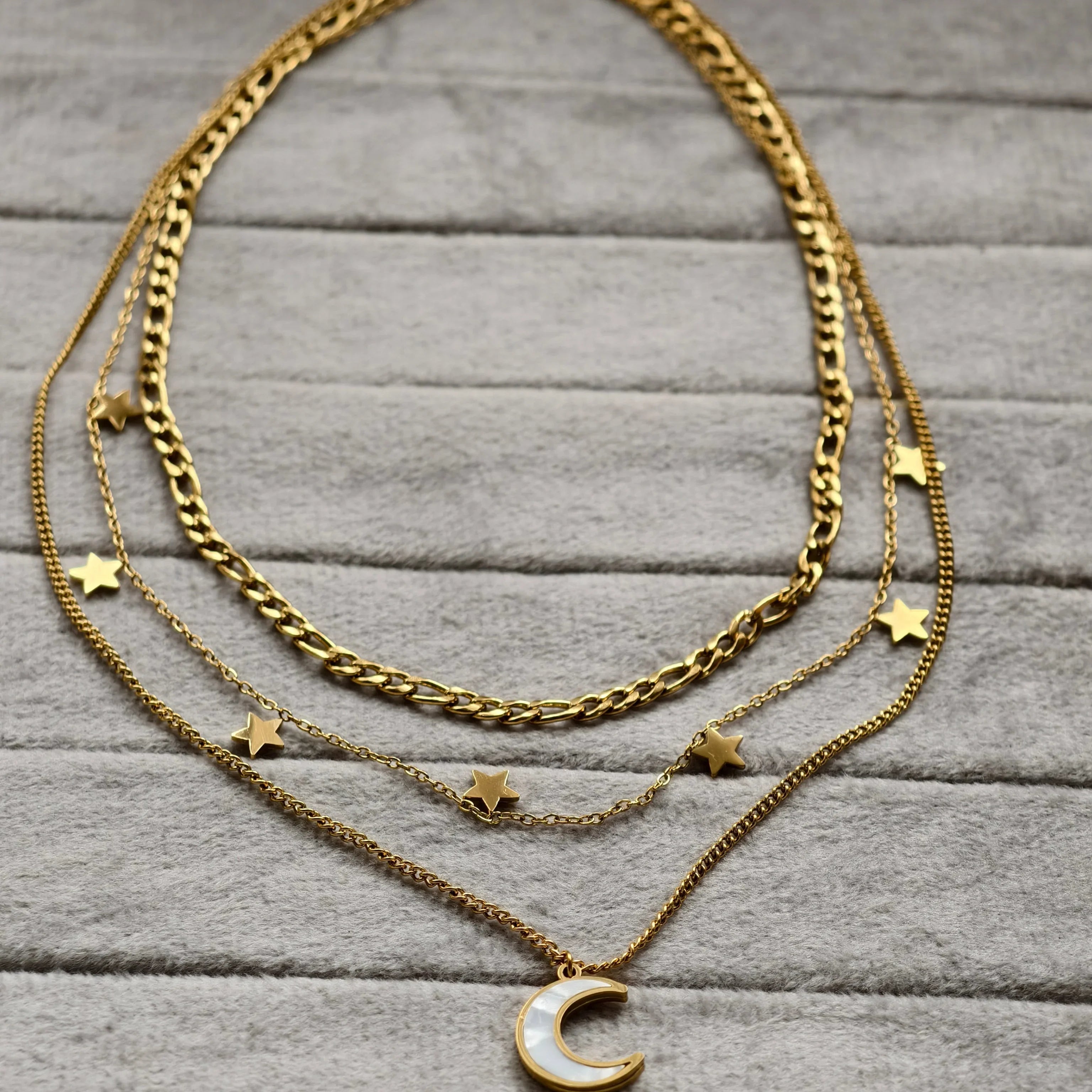 Three-layer gold chain necklaces on gray fabric, featuring stars and a crescent moon pendant