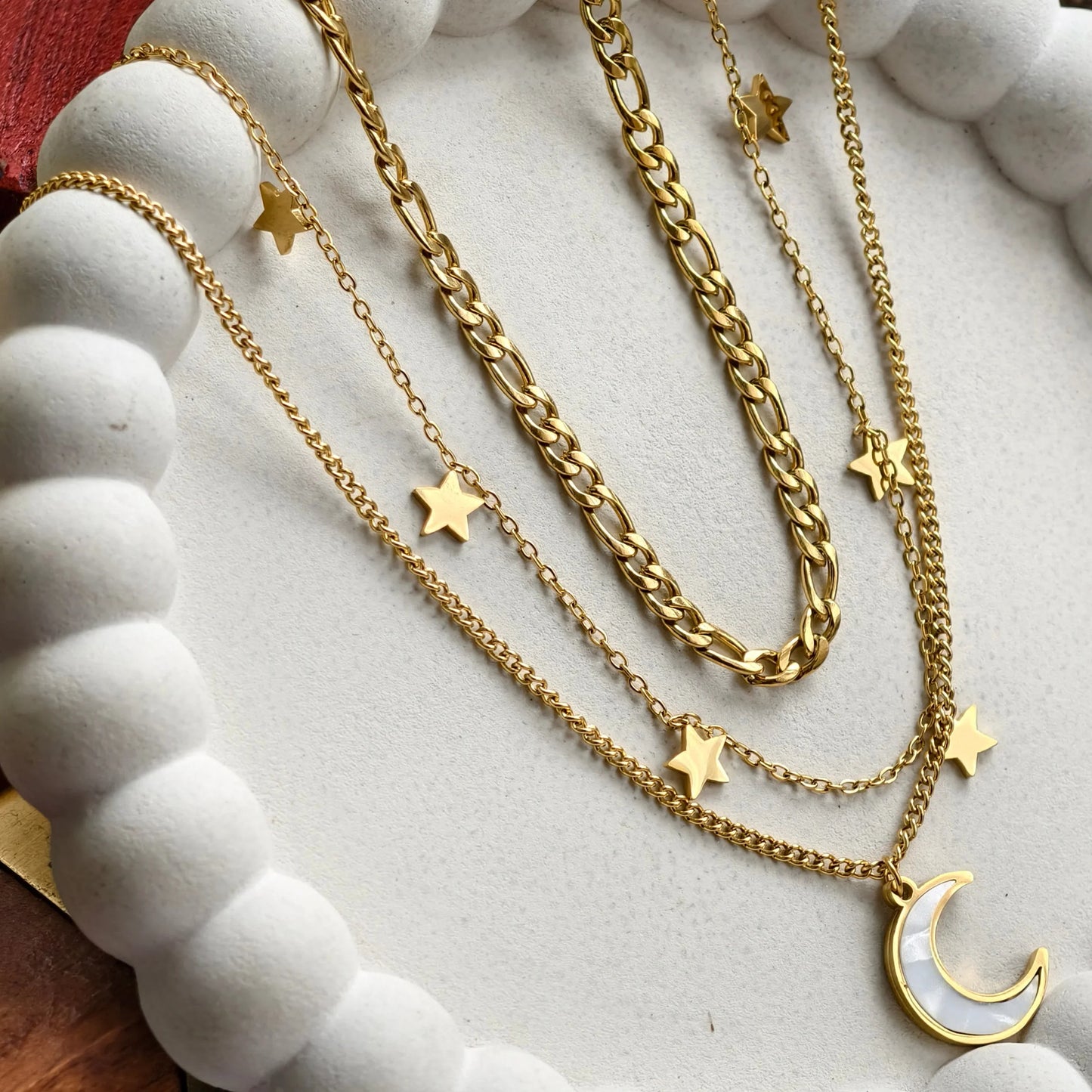 Layered gold chain necklaces with star charms and a crescent moon pendant on white beaded display