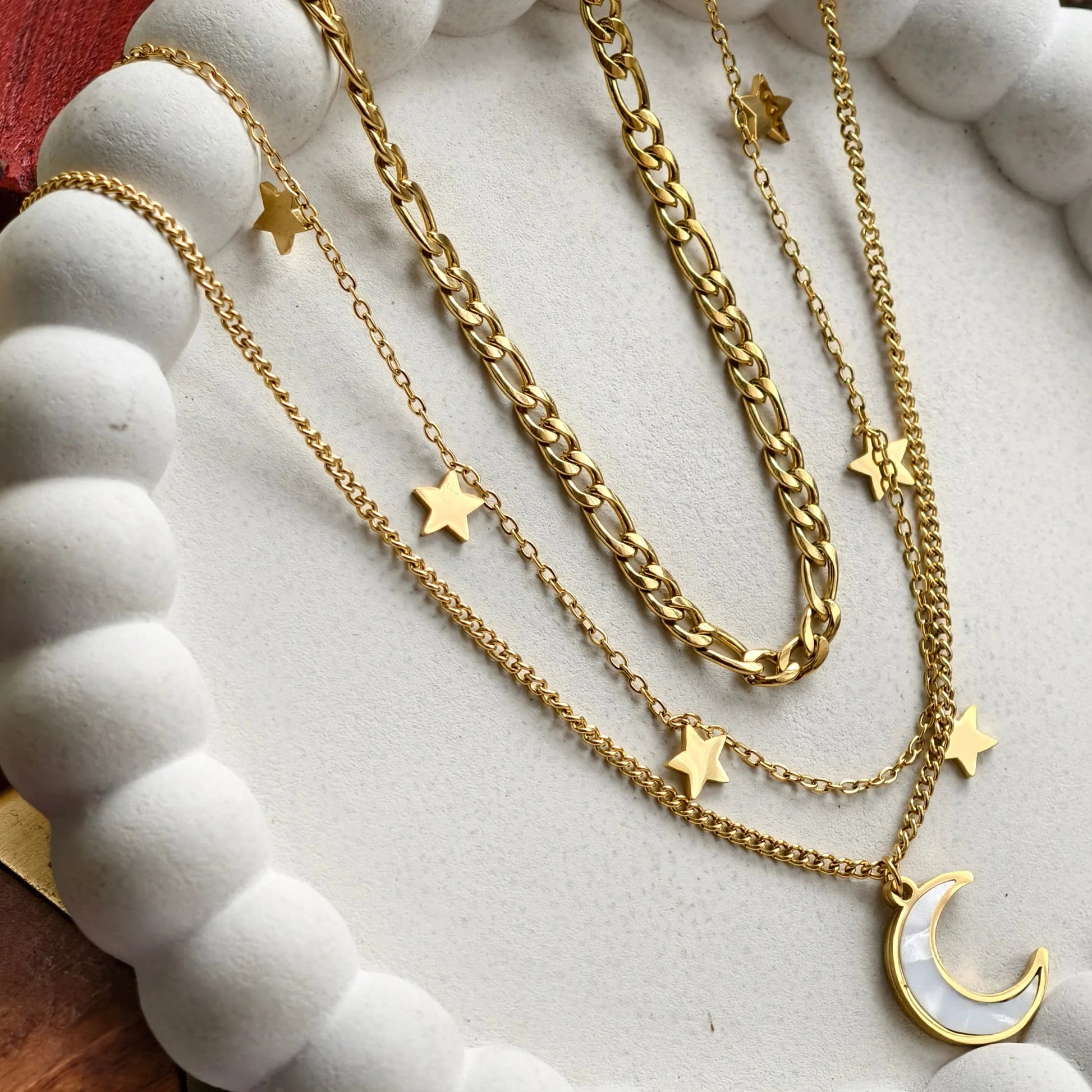 Layered gold chain necklaces with star charms and a crescent moon pendant on white beaded display