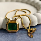 Gold necklace with octagonal green gemstone pendant on blue surface with white textured dish
