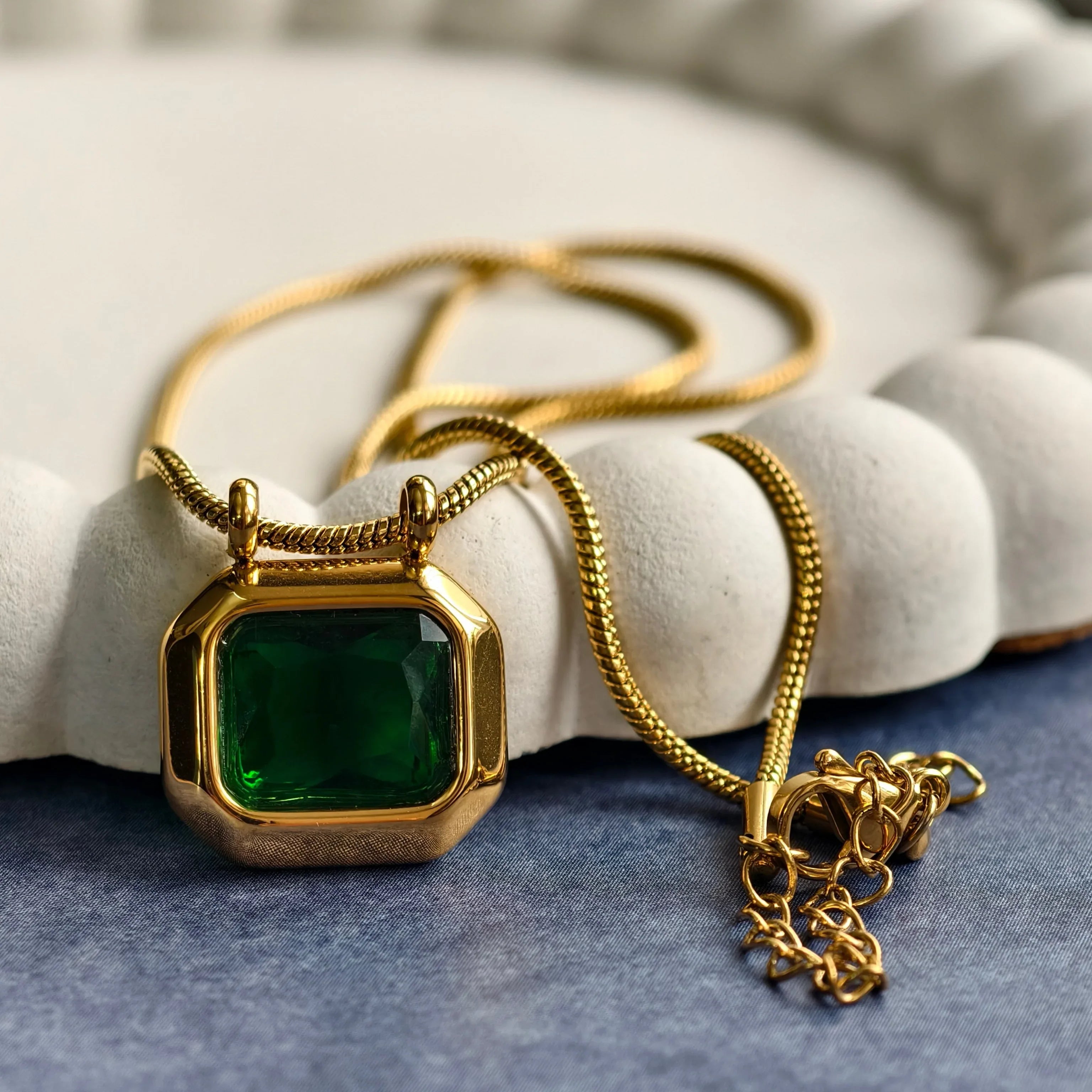 Gold necklace with octagonal green gemstone pendant on blue surface with white textured dish