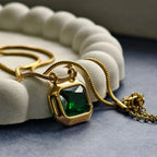Gold pendant necklace with large green gemstone on white textured display and dark surface
