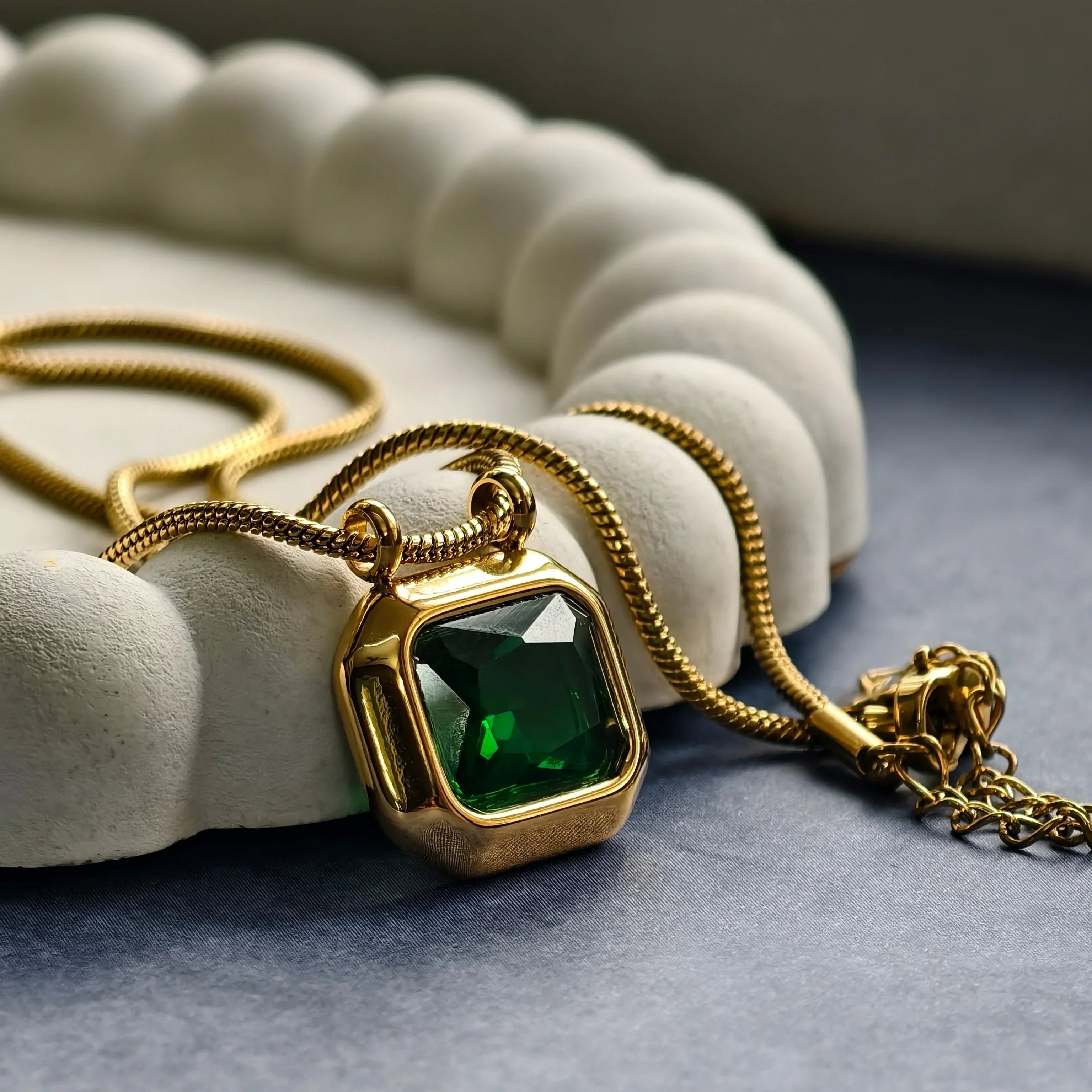 Gold pendant necklace with large green gemstone on white textured display and dark surface
