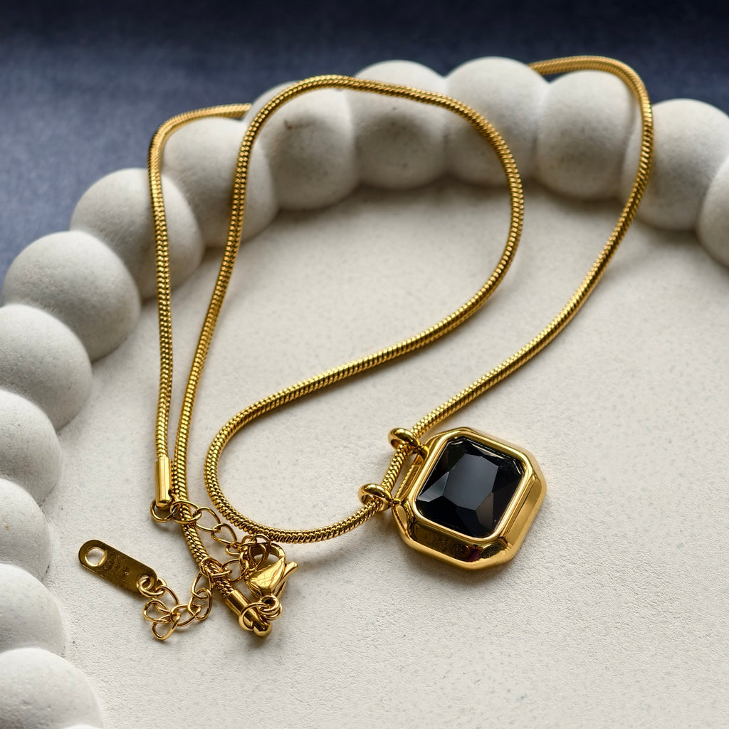 Gold chain necklace with black gemstone pendant displayed on white textured tray