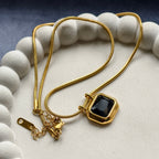 Gold chain necklace with black gemstone pendant displayed on white textured tray