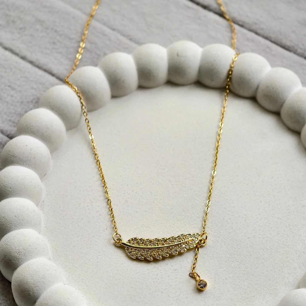 Gold feather necklace with embedded crystals on white textured circular dish