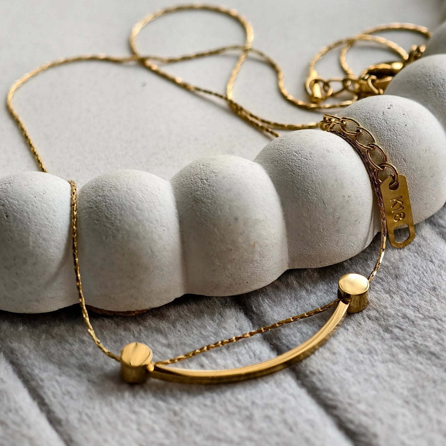 Elegant 18K gold curved bar necklace on textured white and gray background