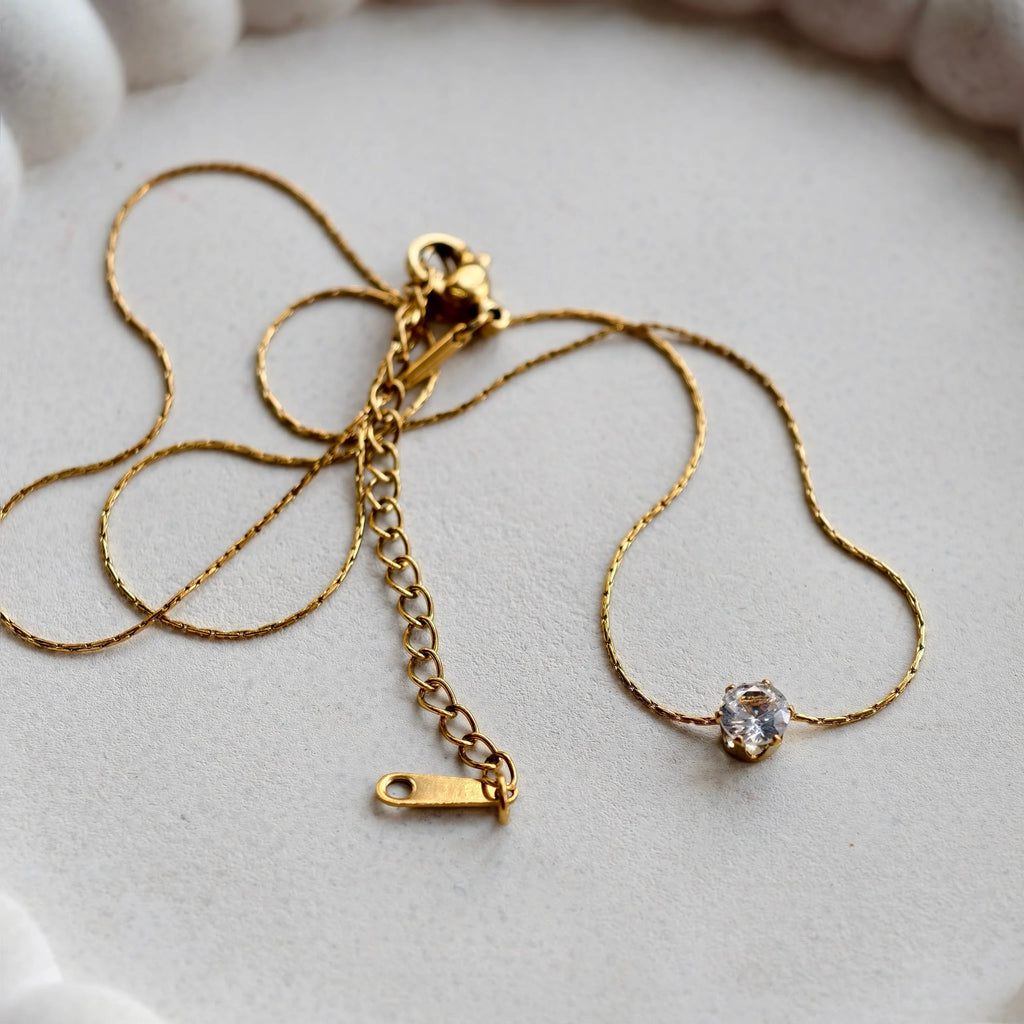 Gold necklace with a clasp on a white ceramic dish