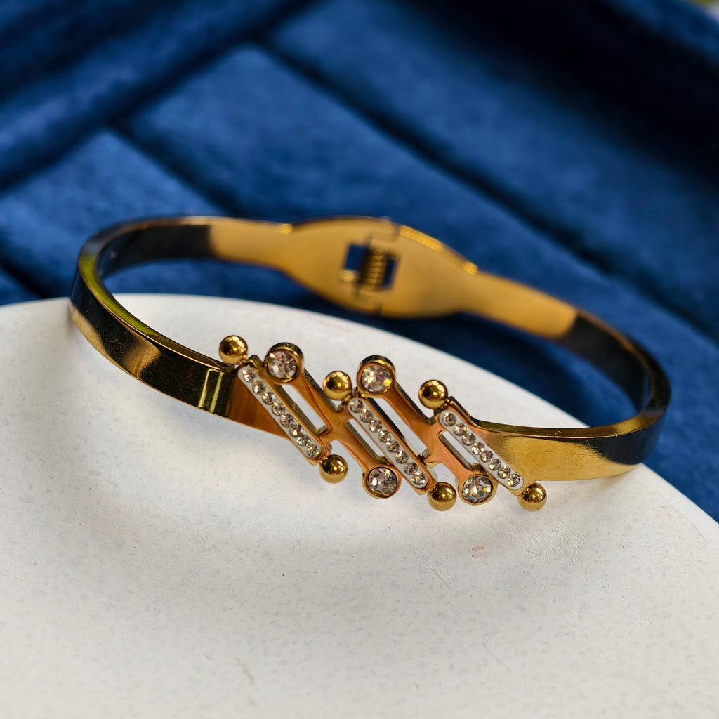 Gold bracelet with black band on a white surface with blue background