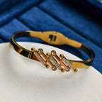 Gold bracelet with black band on a white surface with blue background