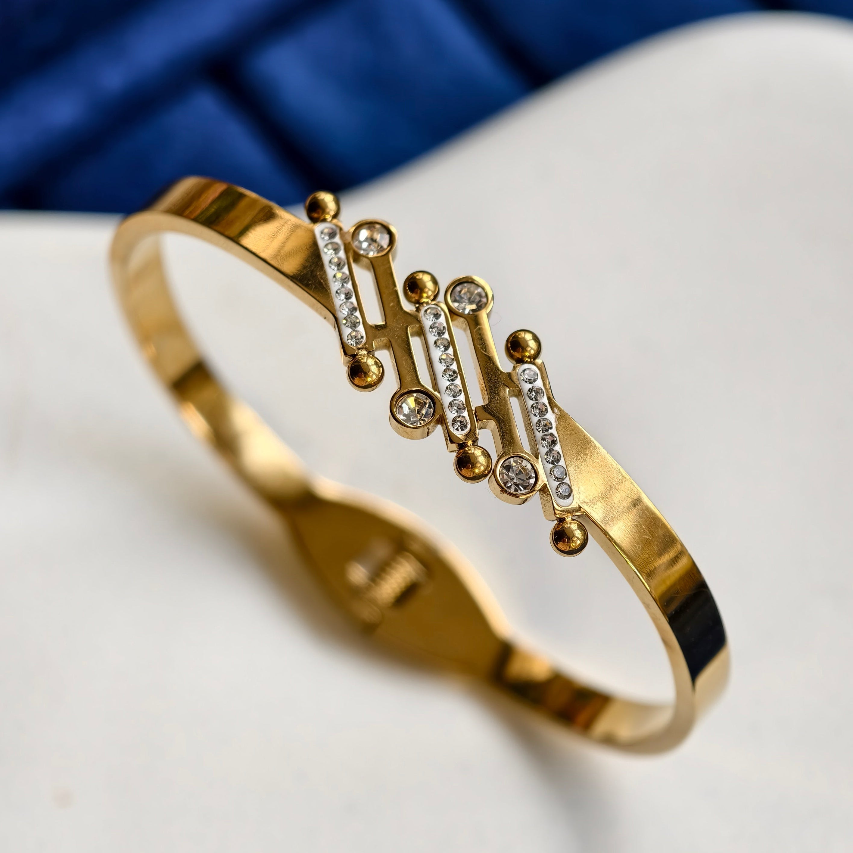 Gold bracelet with diamond accents on a white surface with blue background