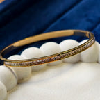 Gold bracelet with small stones on a white stand against a blue fabric background