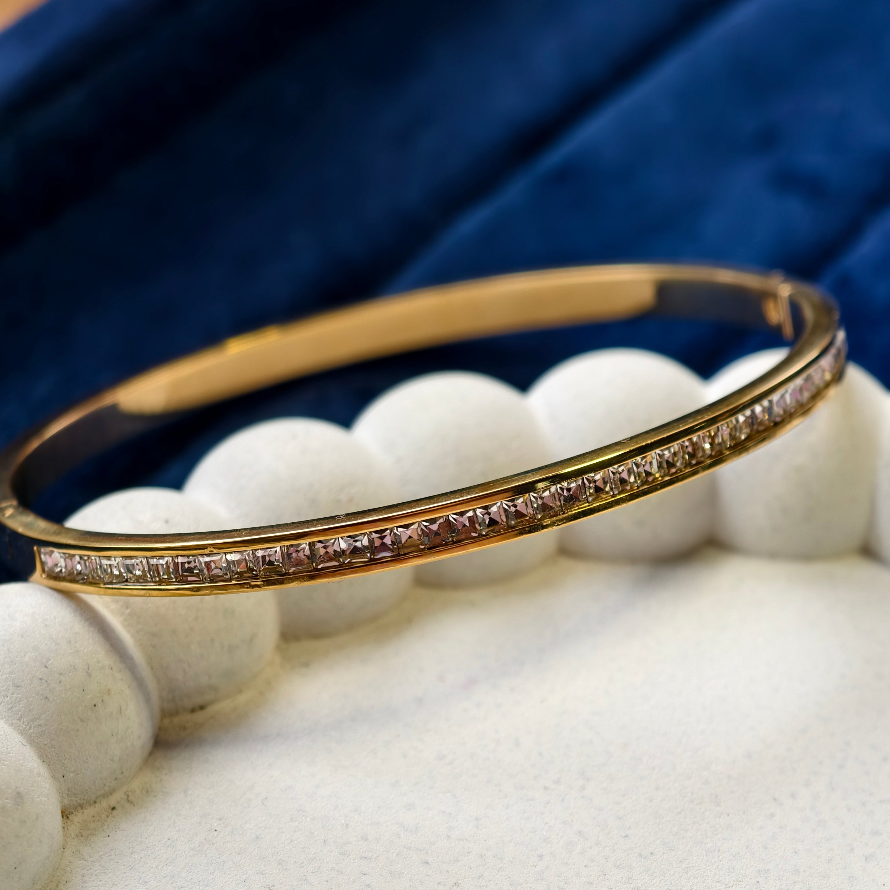 Gold bracelet with small stones on a white stand against a blue fabric background