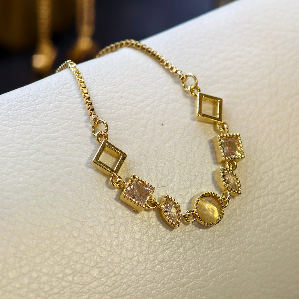 Gold bracelet with square and round charms on a white surface