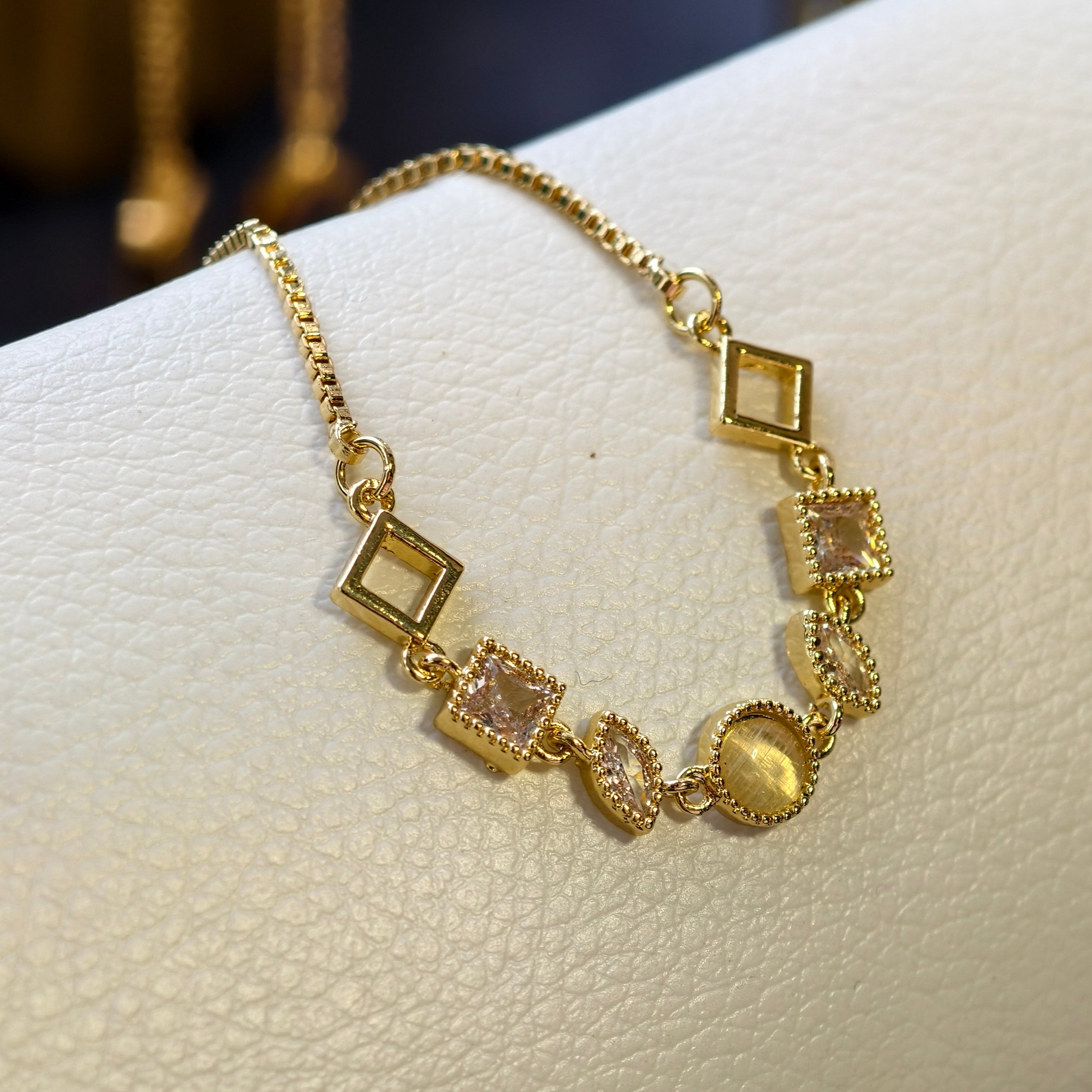 Gold bracelet with square and round charms on a white surface