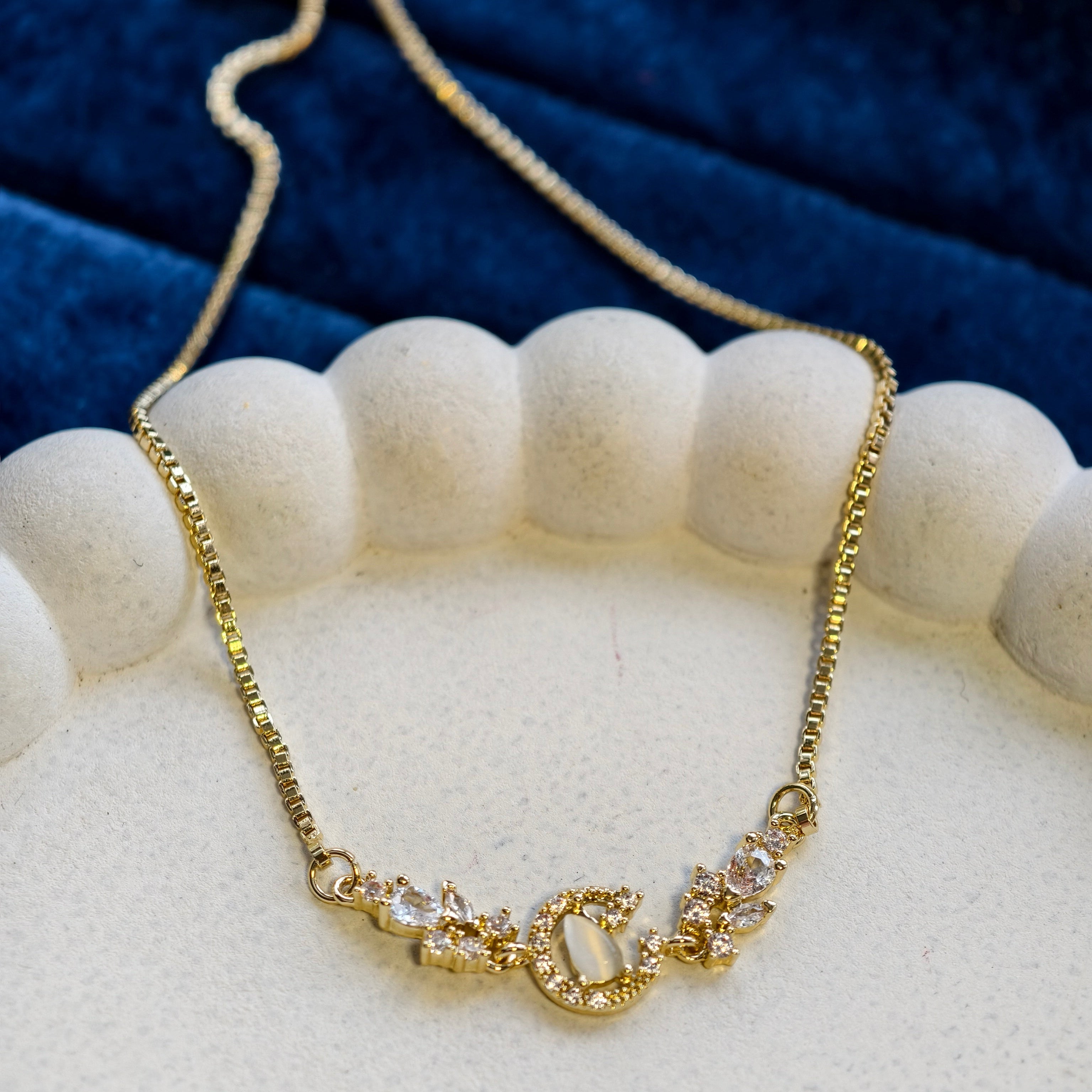 Gold necklace with a decorative clasp on a white stand against a blue fabric background